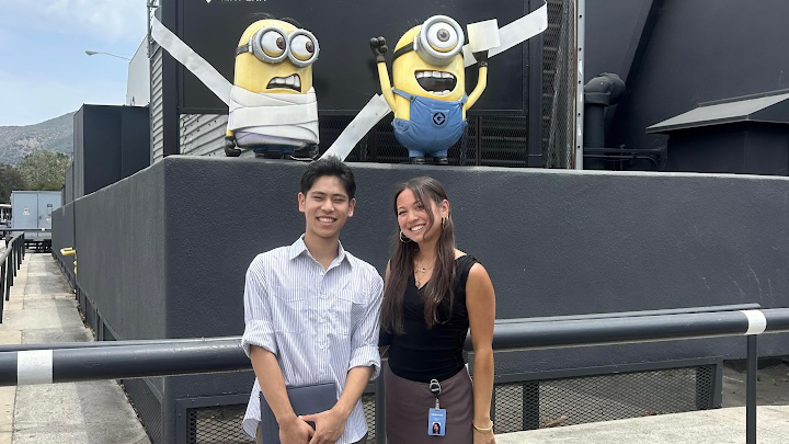 Alt text: Two interns standing and smiling in front of large Minions figures on a studio lot.