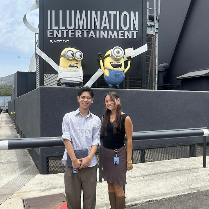 Alt text: Two interns standing and smiling in front of large Minions figures on a studio lot.